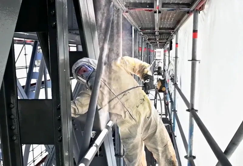 Man spraying paint on bridge structures