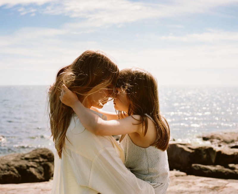 mother and daughter hugging on rocky beach under sun