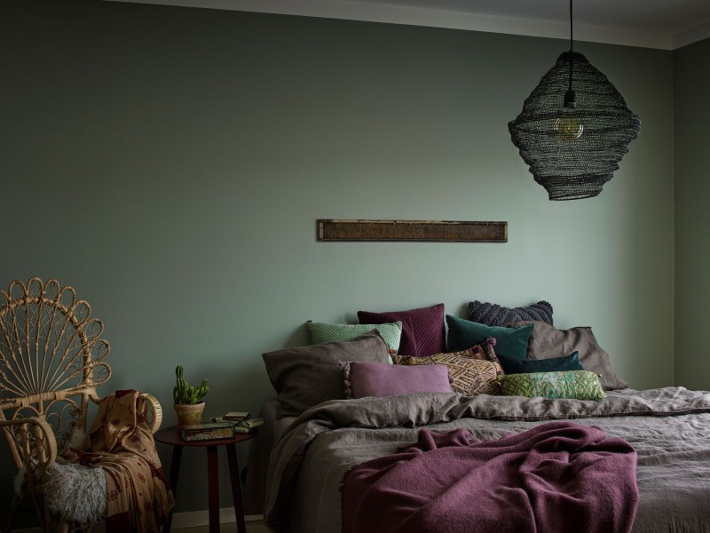 green colour accent wall in bedroom with bohemian style pillows and lamp